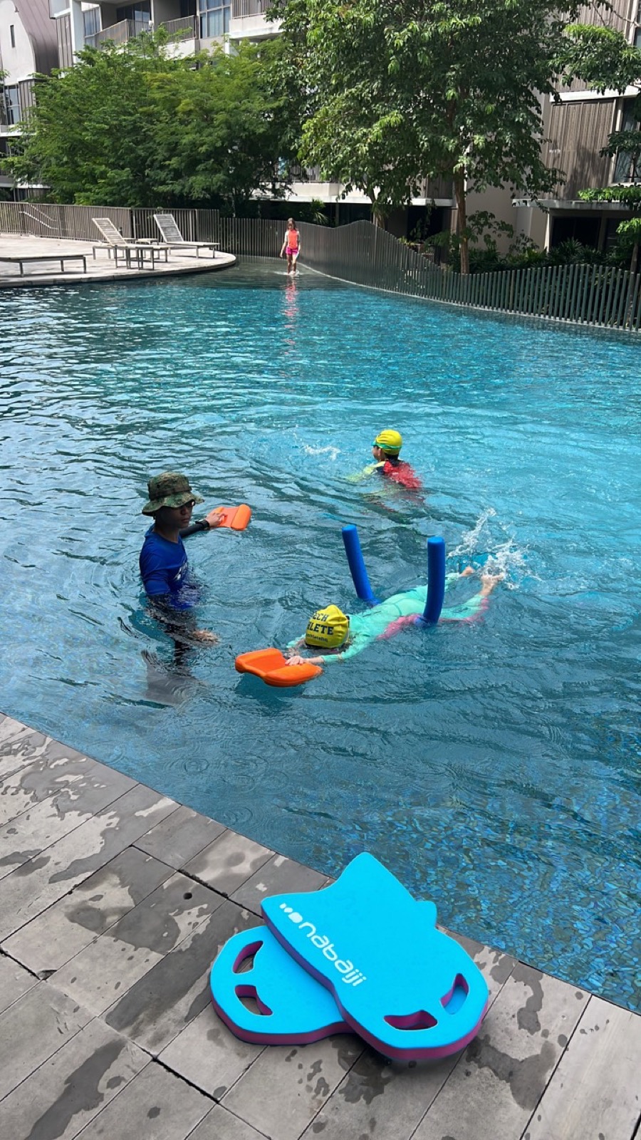 Penguin Swim School coach supervising two children practising water-confidence drills at a Singapore condo pool